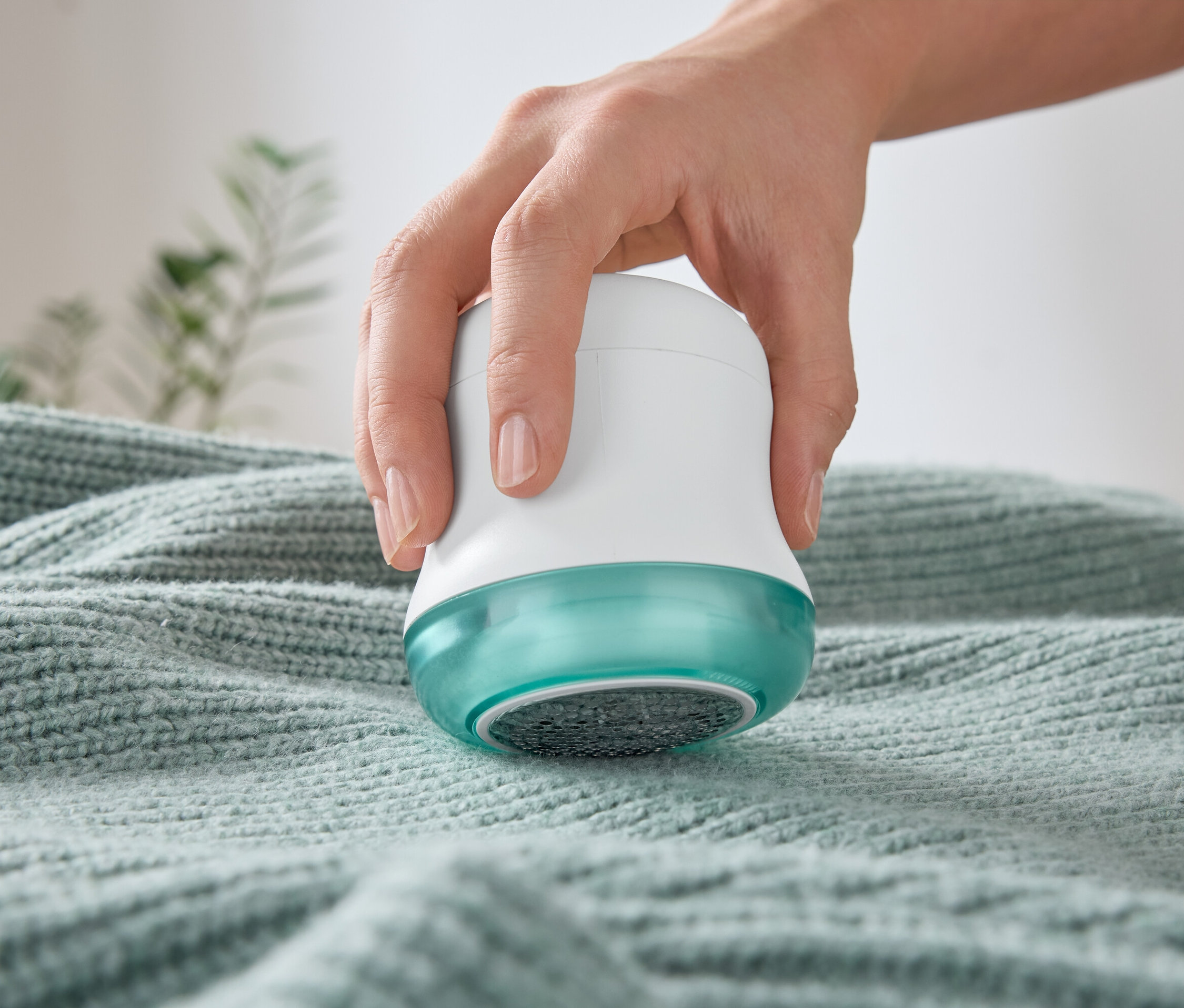 Ręka używa golarki do ubrań na swetrze.