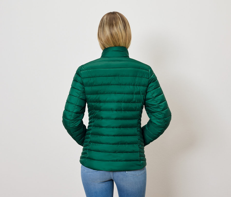 Widok z tyłu na kobietę z blond włosami w zielonej pikowanej kurtce i niebieskich dżinsach.