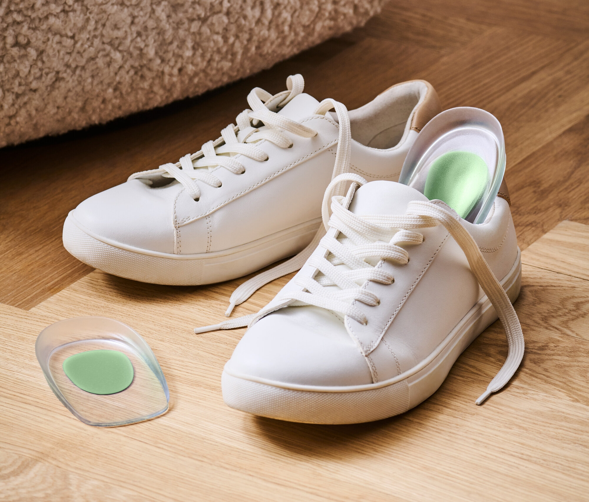 Dwa białe trampki leżą na drewnianej podłodze, jeden z zieloną wkładką.