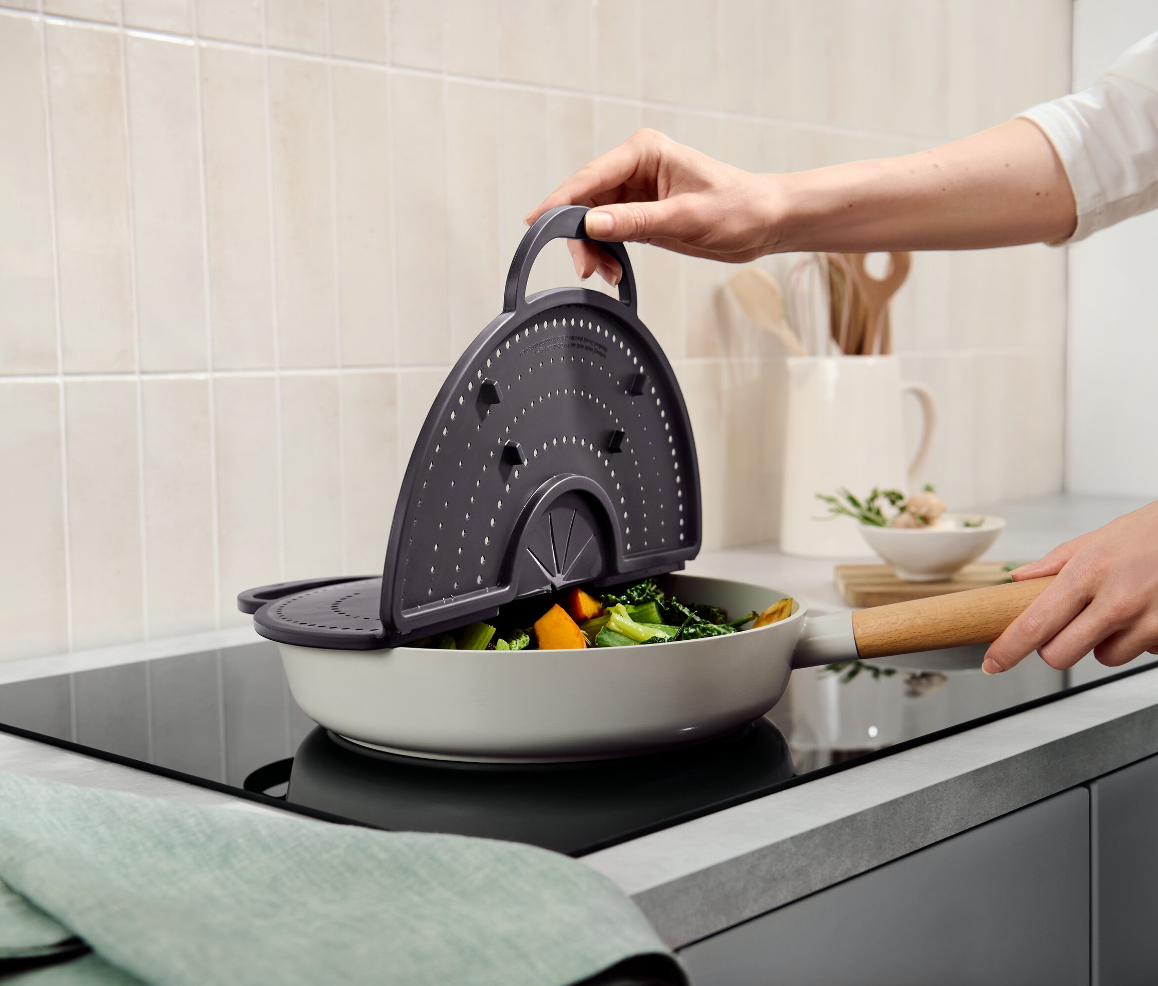 Ręka trzyma szare sitko nad patelnią z warzywami.