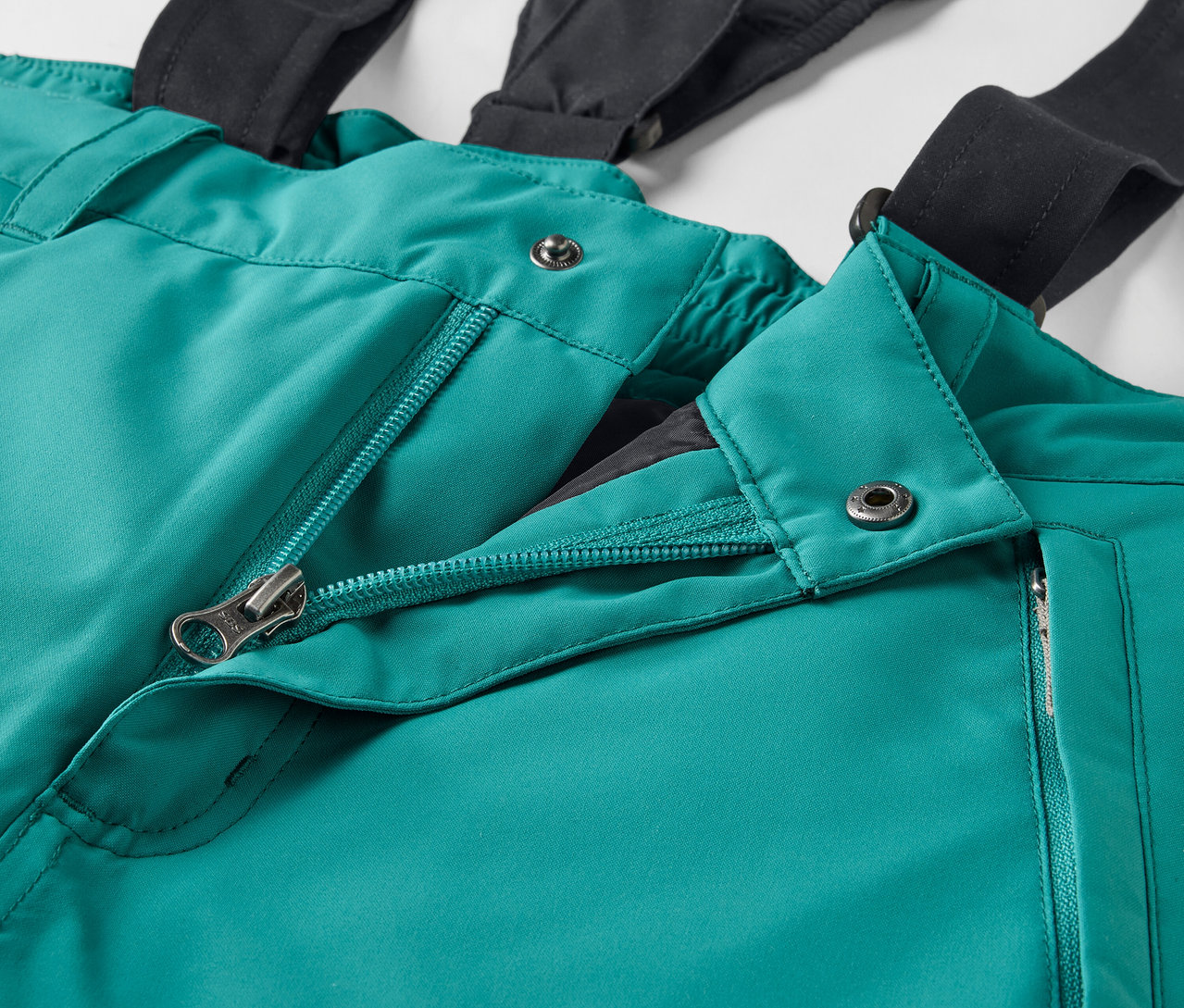 Szczegół zielonych spodni narciarskich z czarnymi szelkami i otwartym zamkiem błyskawicznym.