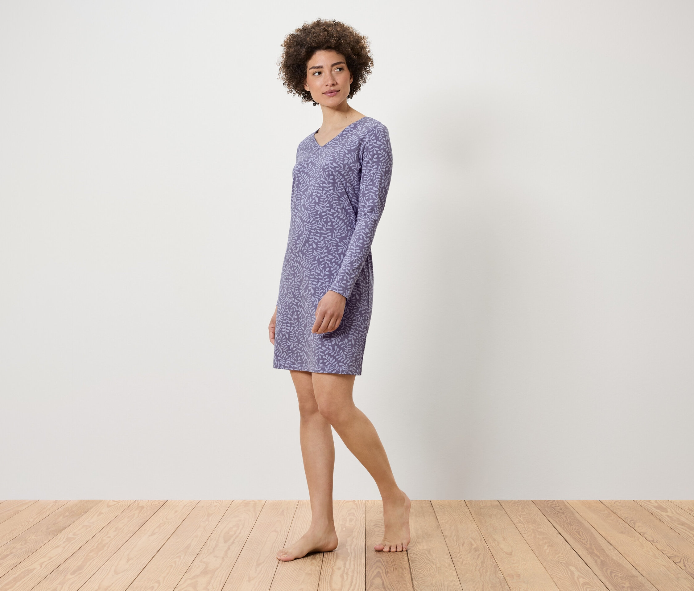 Kobieta pozuje w liliowej sukience z długim rękawem i roślinnym wzorem.