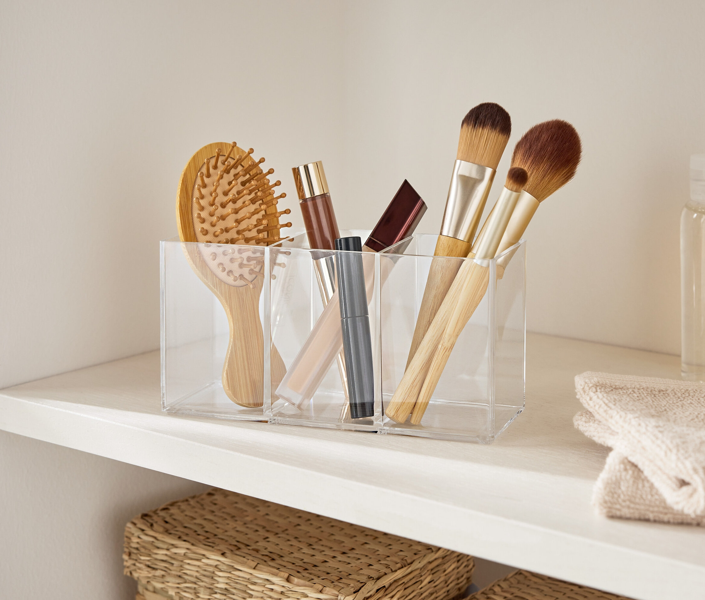 Szczotka do włosów i pędzle do makijażu w przezroczystym akrylowym organizerze na białej półce.