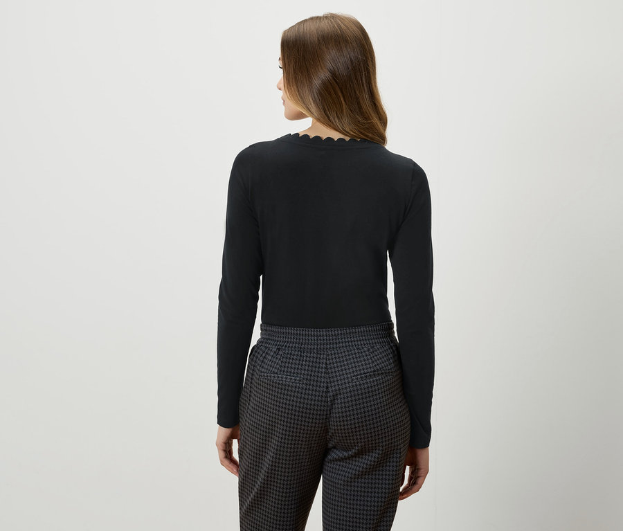 Widok z tyłu na kobietę z brązowymi włosami w czarnej bluzce z długim rękawem i szaro-czarnych spodniach.