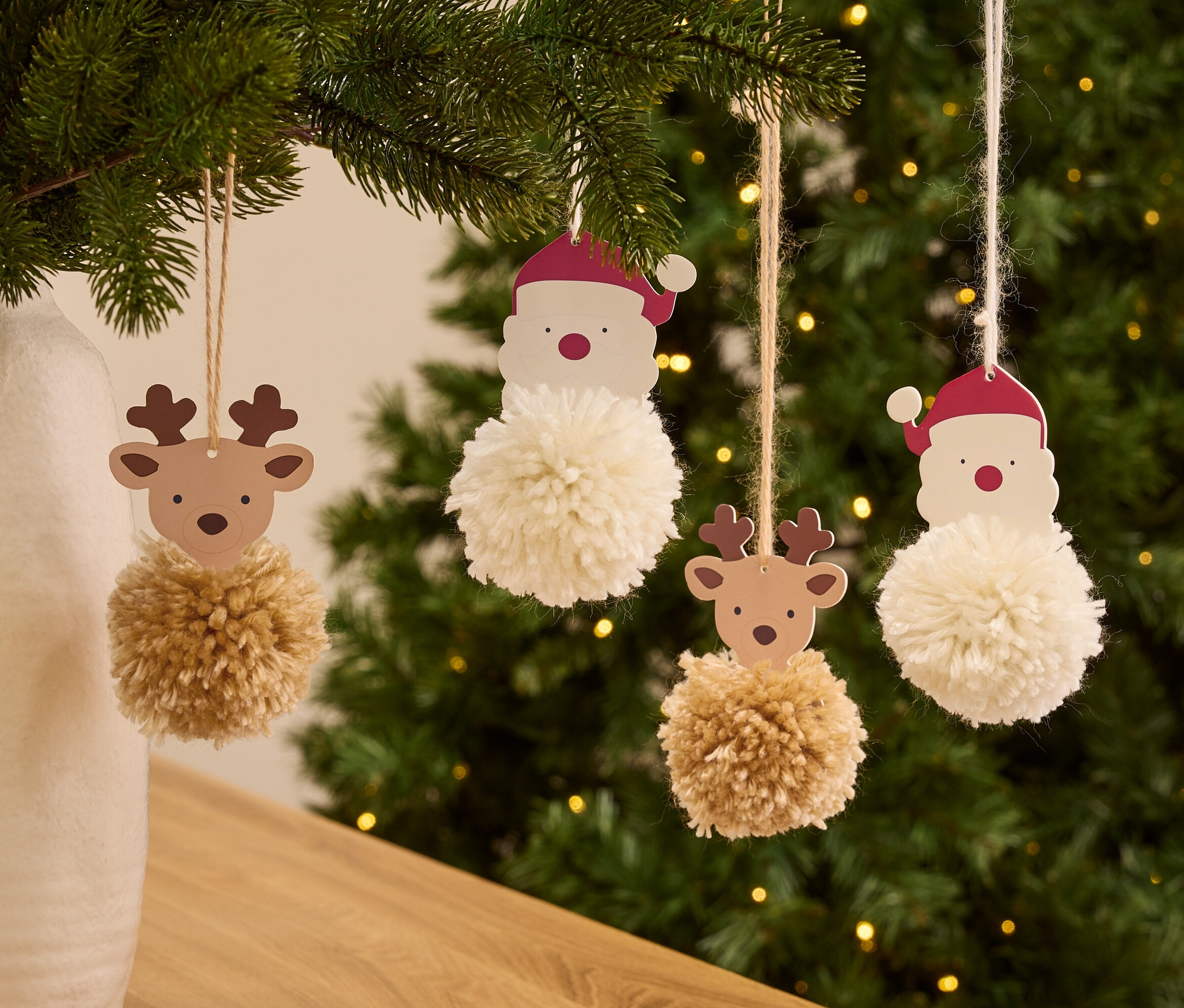 Na choince wiszą ozdoby Świętego Mikołaja i renifera z pomponami.