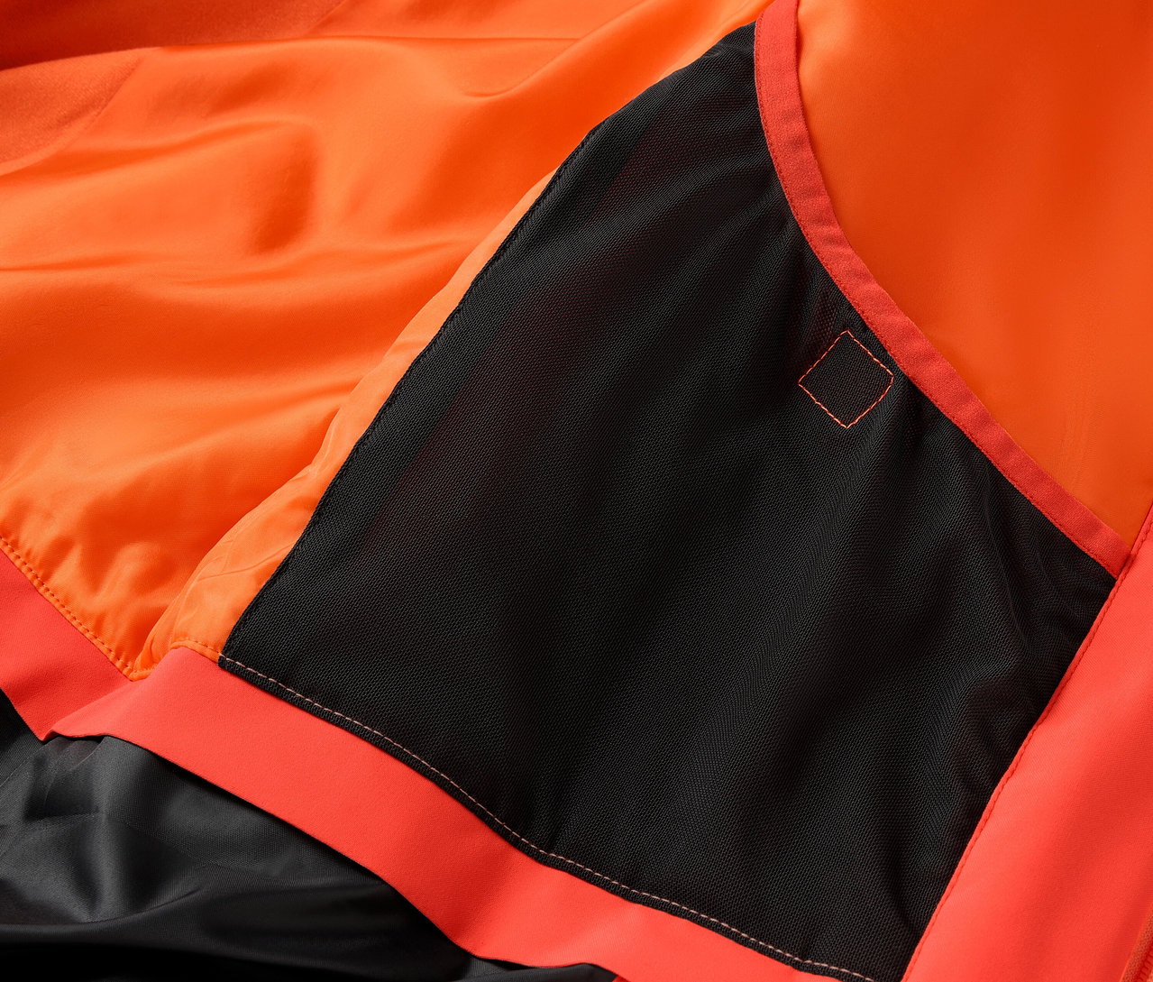 Szczegół pomarańczowej kurtki z czarną kieszenią.