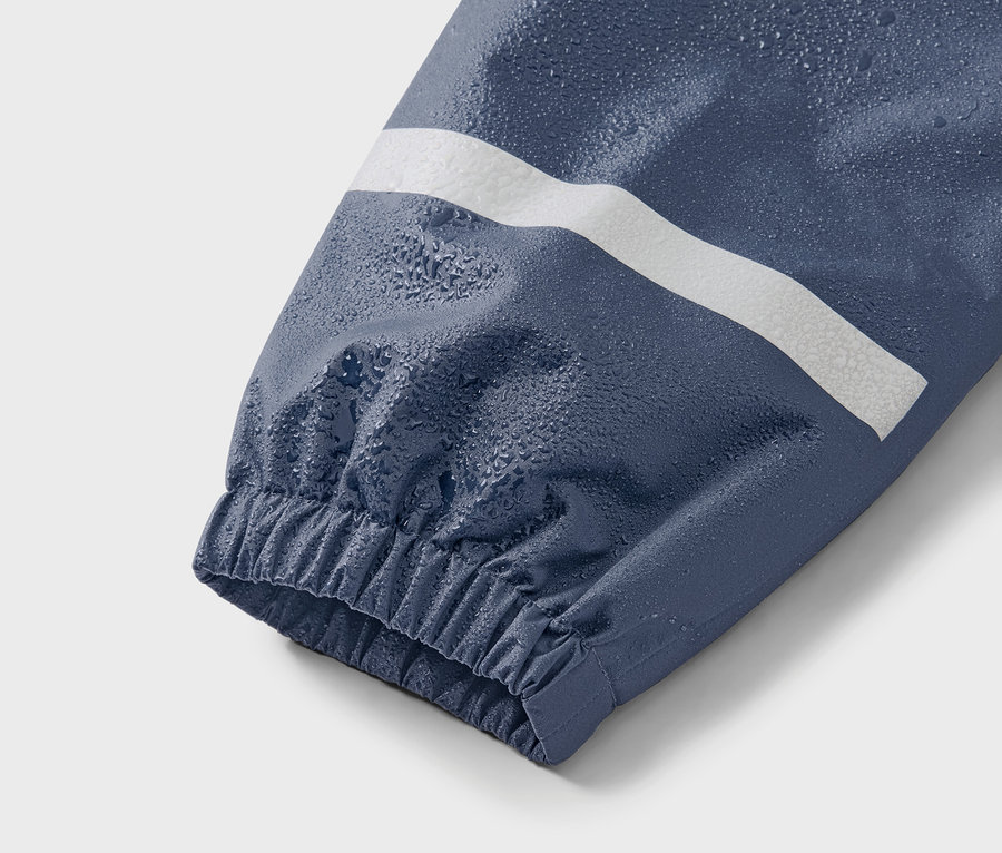 Zbliżenie na niebieski rękaw kurtki z białym paskiem i kroplami wody.