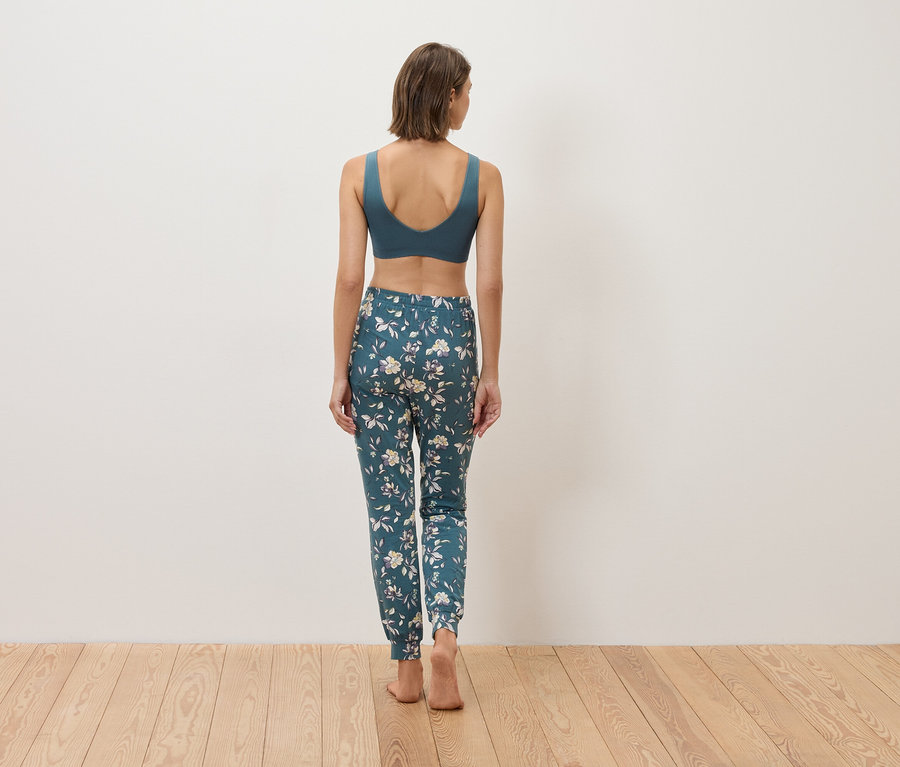 Widok z tyłu kobiety w niebieskim staniku sportowym i kwiecistych spodniach na drewnianej podłodze.