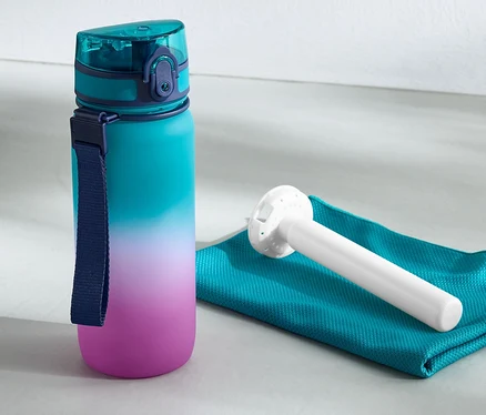 Bidon z wkładem chłodzącym stoi obok ręcznika i odważnika kettlebell.