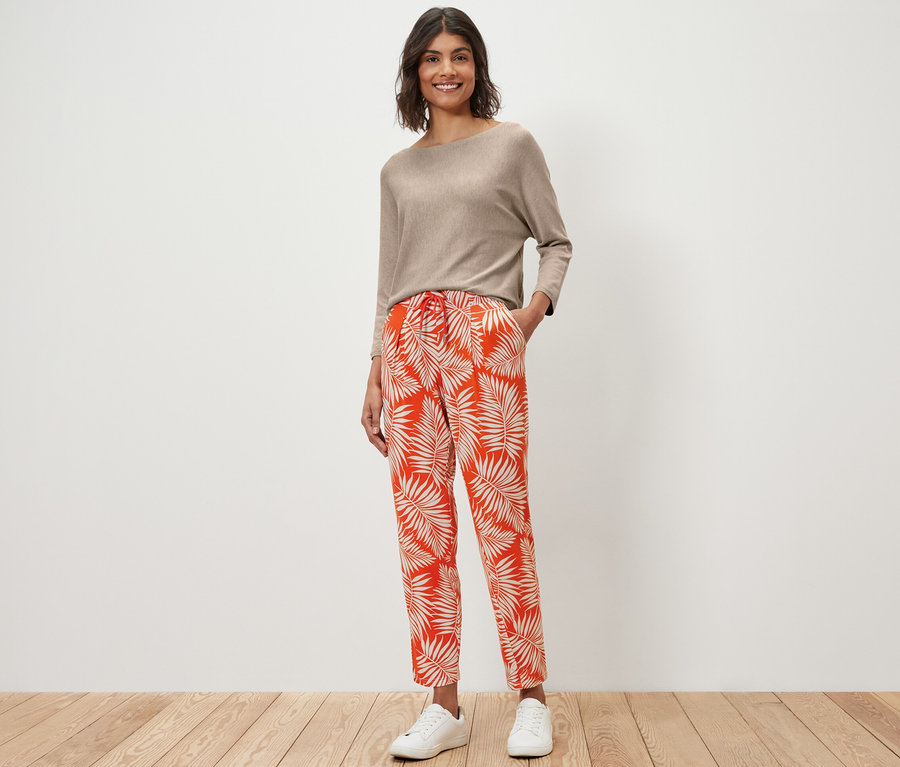 Kobieta stoi w beżowej bluzce i wzorzystych spodniach z dżerseju.
