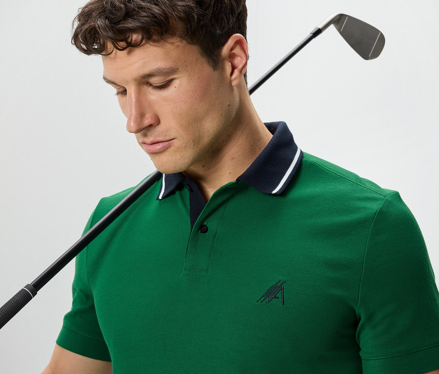 Mężczyzna z kijem golfowym na ramieniu ma na sobie zieloną koszulkę polo.