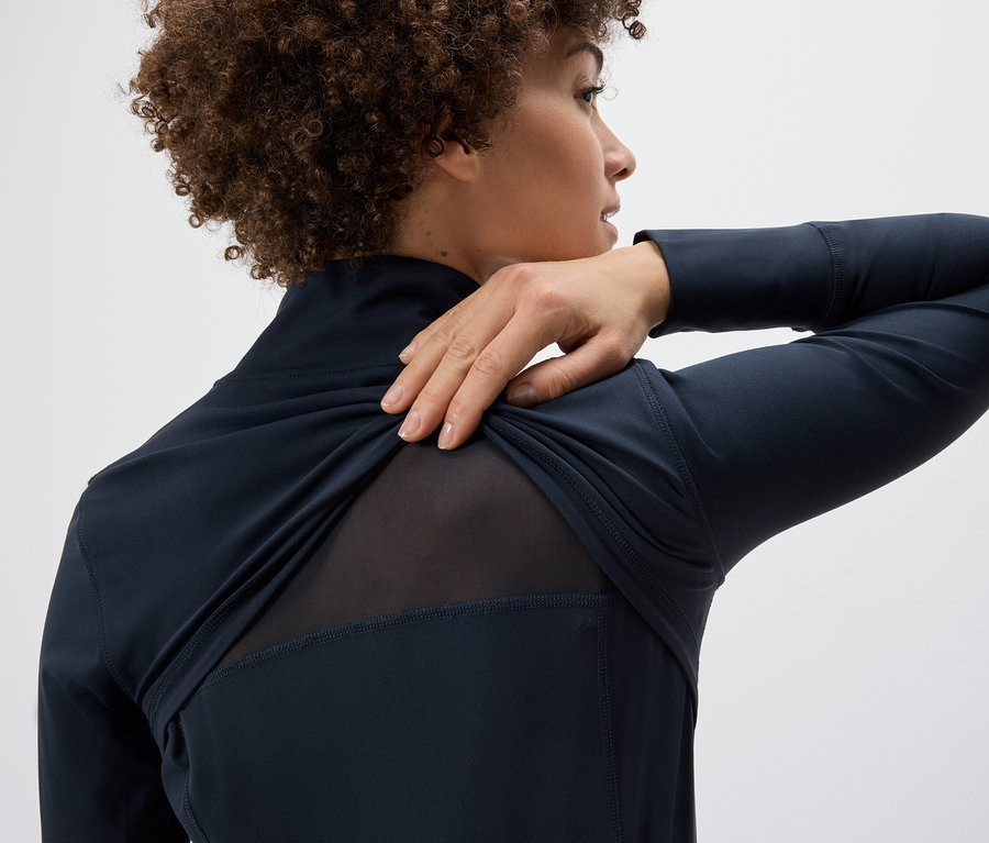 Kobieta naciąga bluzę funkcyjną na ramię, ukazując siateczkowy panel na plecach.