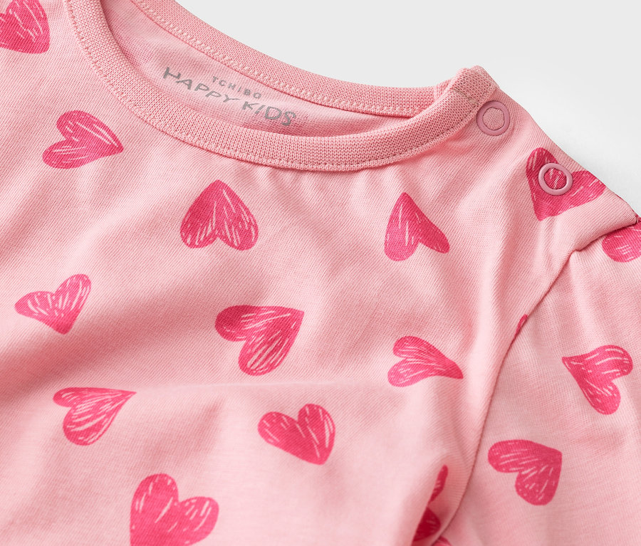 Zbliżenie na różową koszulkę z długim rękawem, wzorem w serca i zatrzaskami przy kołnierzu.