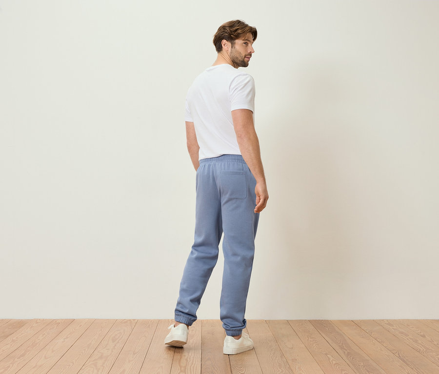 Mężczyzna w jasnoniebieskich spodniach dresowych i białym t-shircie, widziany od tyłu.
