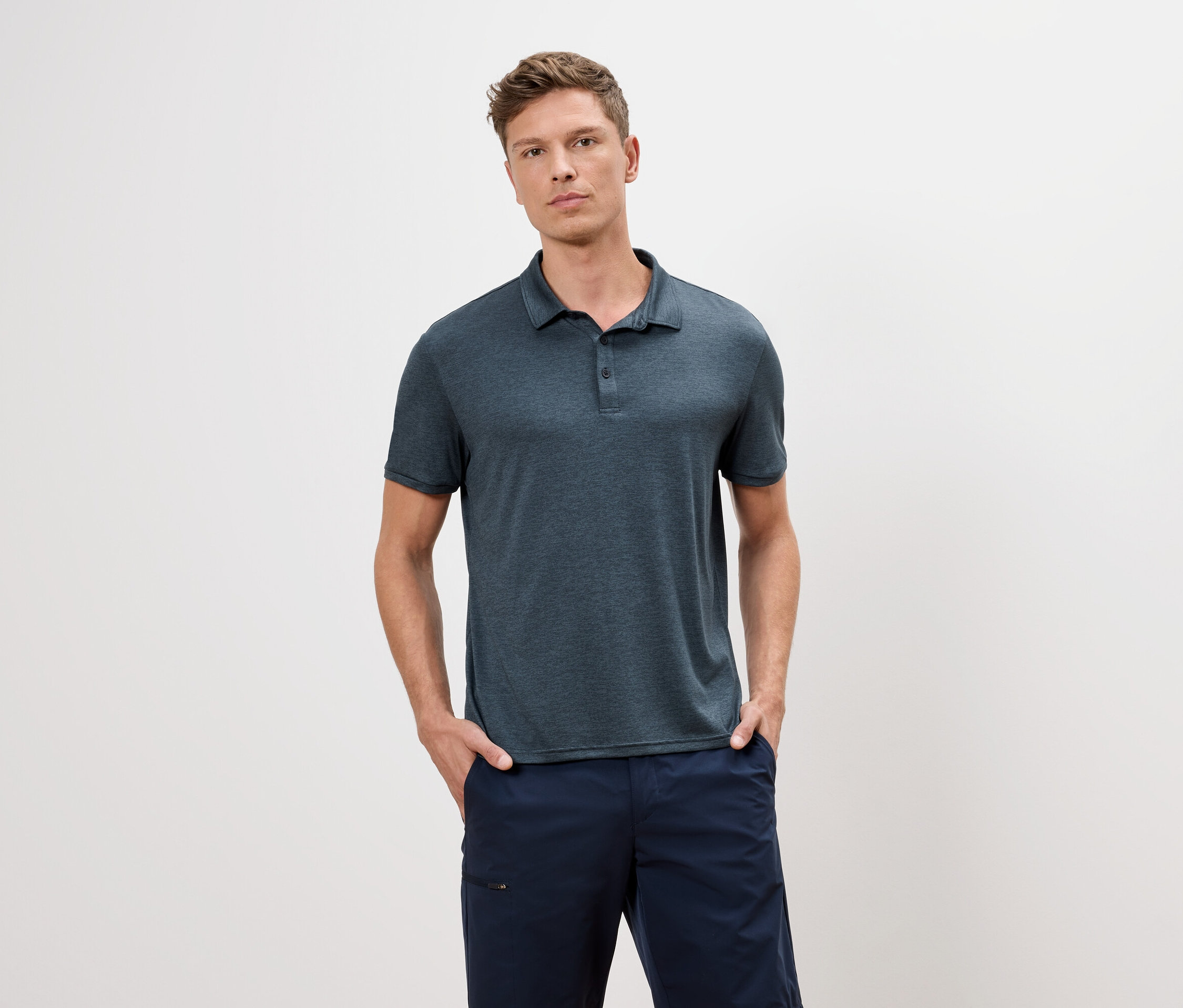 Mężczyzna w niebieskiej koszulce polo i niebieskich szortach stoi na białym tle.