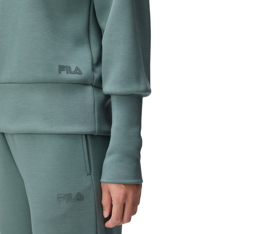 Zbliżenie osoby ubranej w turkusowy dres marki Fila, z logo Fila widocznym na górze i spodniach.