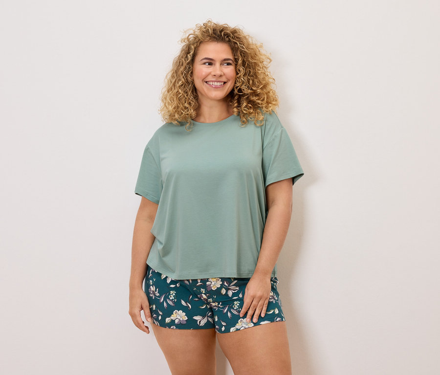 Kobieta z kręconymi włosami w zielonym T-shircie i szortach w kwiaty.