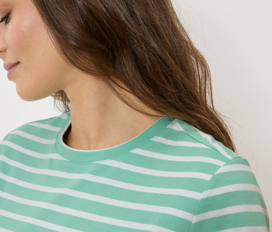 Zbliżenie kobiety o brązowych włosach w zielono-białej koszulce w paski.