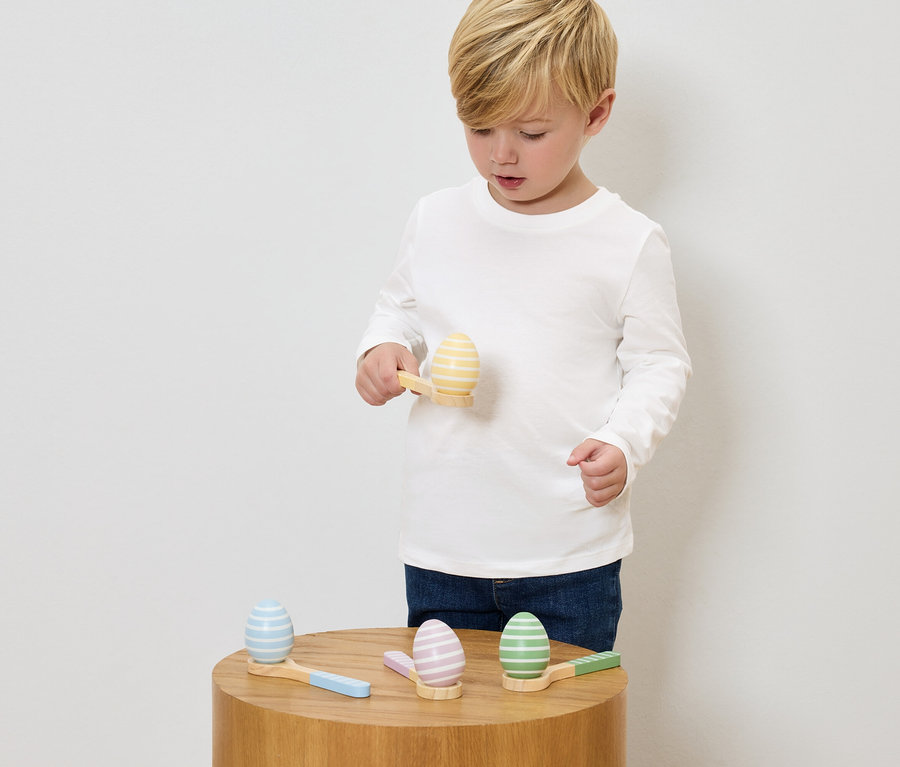 Chłopiec bawi się malowanymi drewnianymi jajkami i małymi młotkami na drewnianym stole.