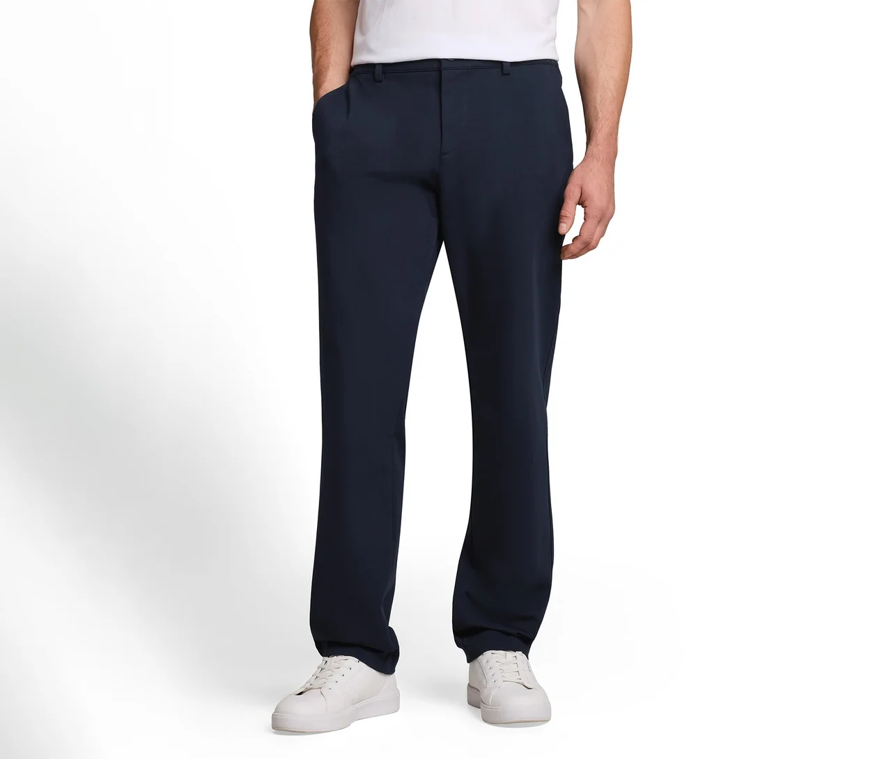 Mężczyzna w ciemnoniebieskich spodniach i białych sneakersach, z jedną ręką w kieszeni.