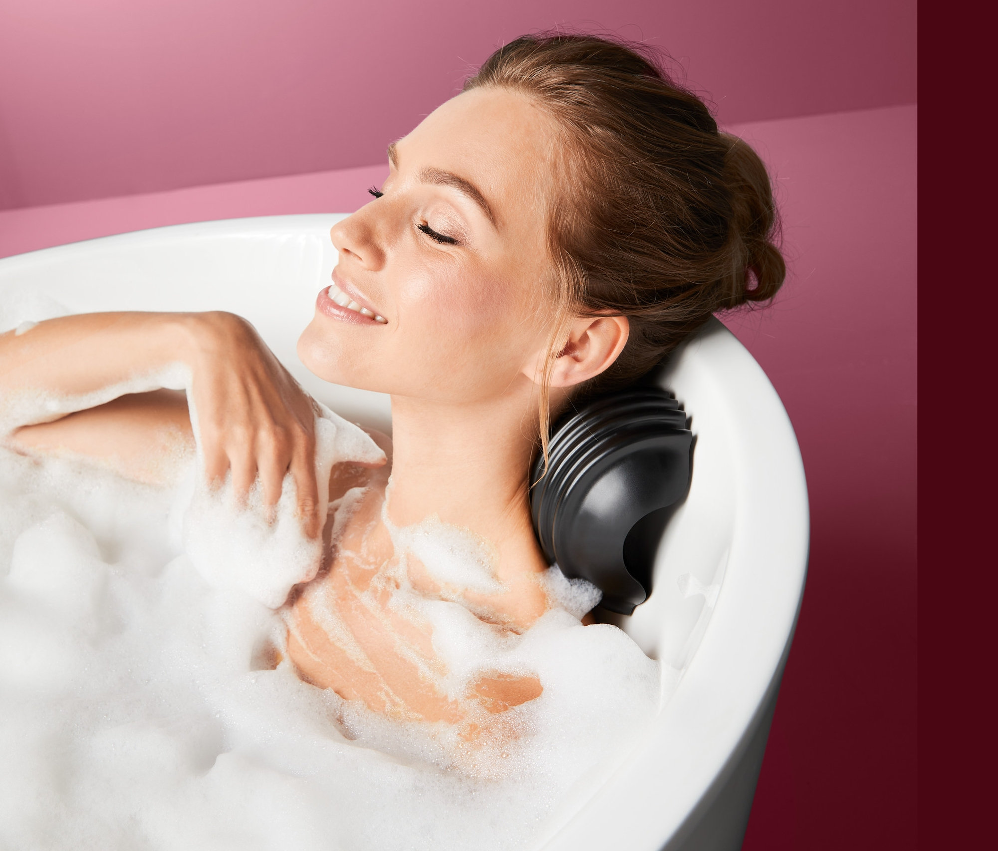 Uśmiechnięta kobieta leży w wannie pełnej piany z poduszką do masażu w wannie.