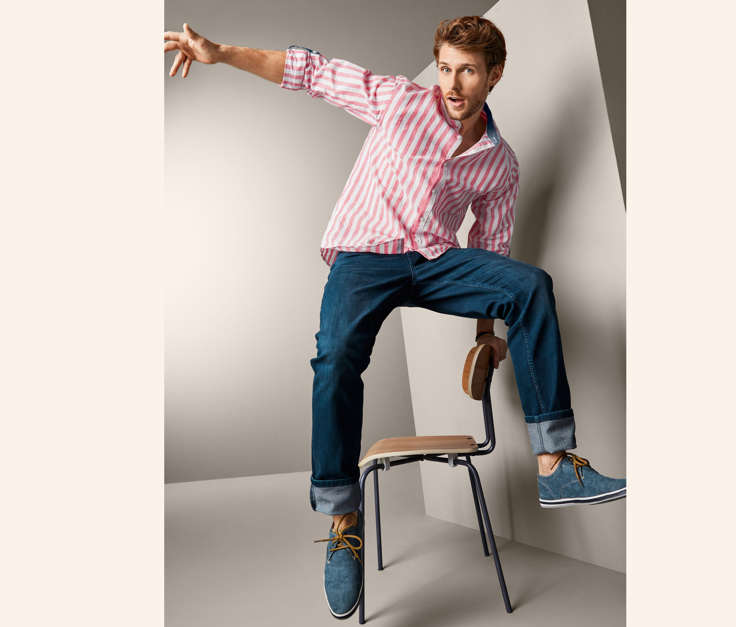 Mężczyzna siedzi na krześle ubrany w bawełniano-lnianą męską koszulę ze stójką, w koralowo-białe paski.