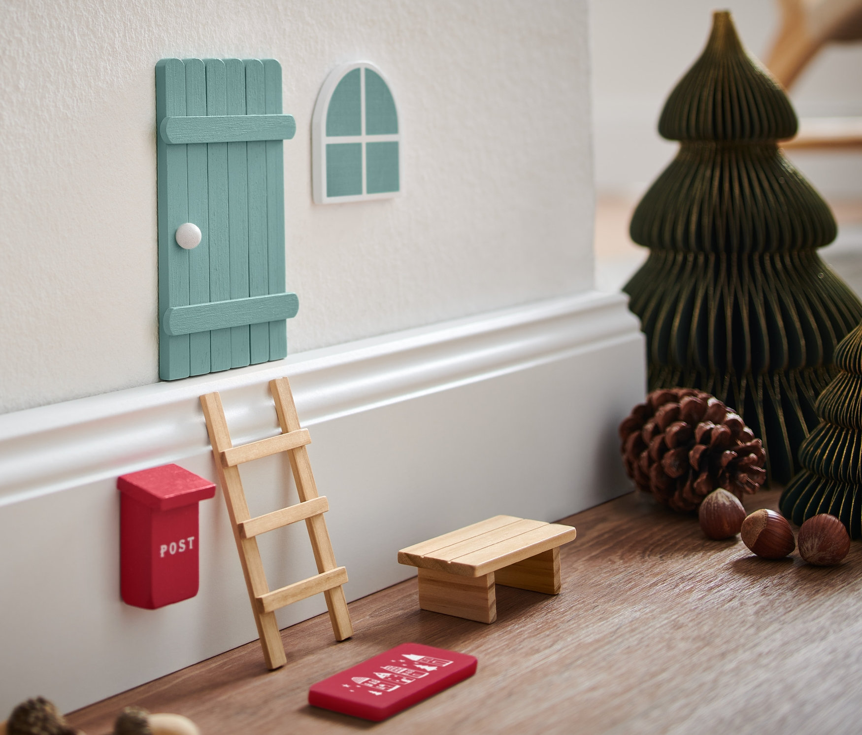 Zestaw dla elfa na ścianie z miniaturowymi choinkami i dekoracjami.