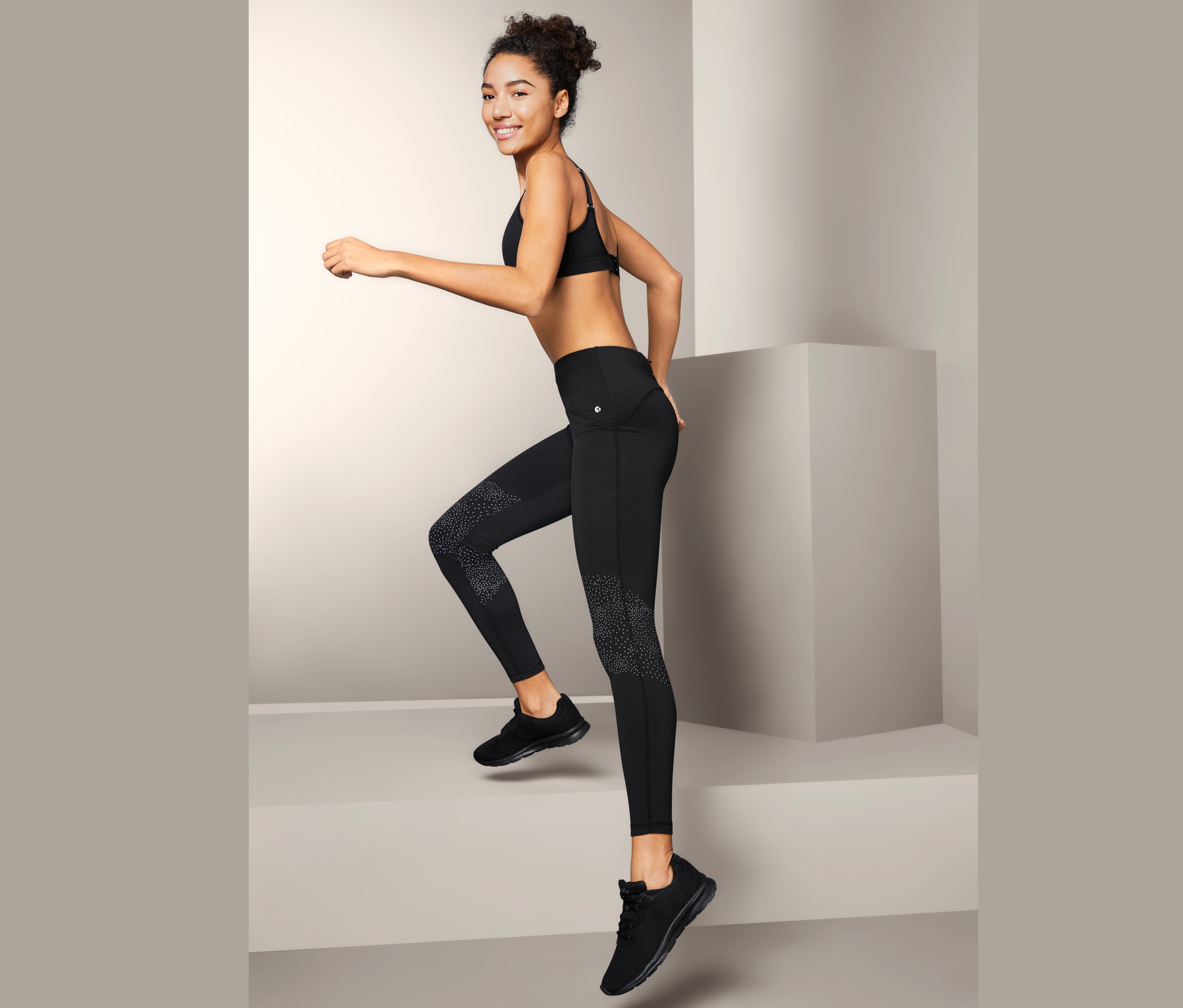 Uśmiechnięta kobieta wchodzi po schodach, ubrana w damskie legginsy sportowe, biustonosz sportowy i tenisówki.