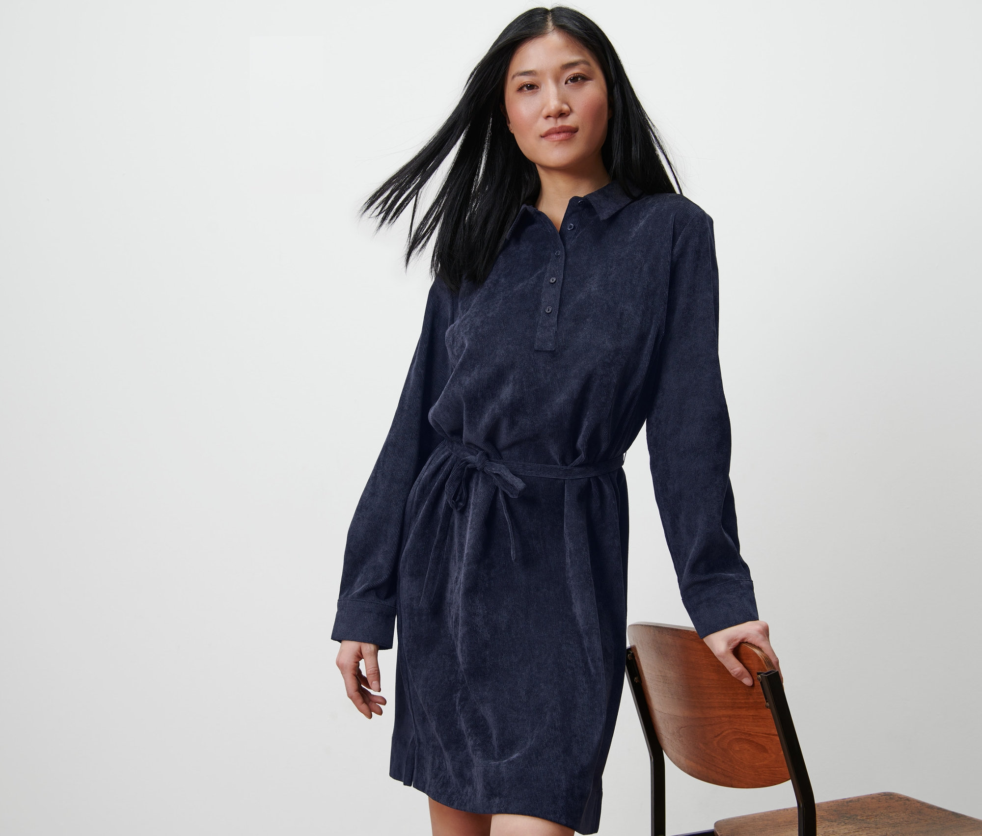 Kobieta pozuje w sukience ze sztruksu, opierając się o krzesło.