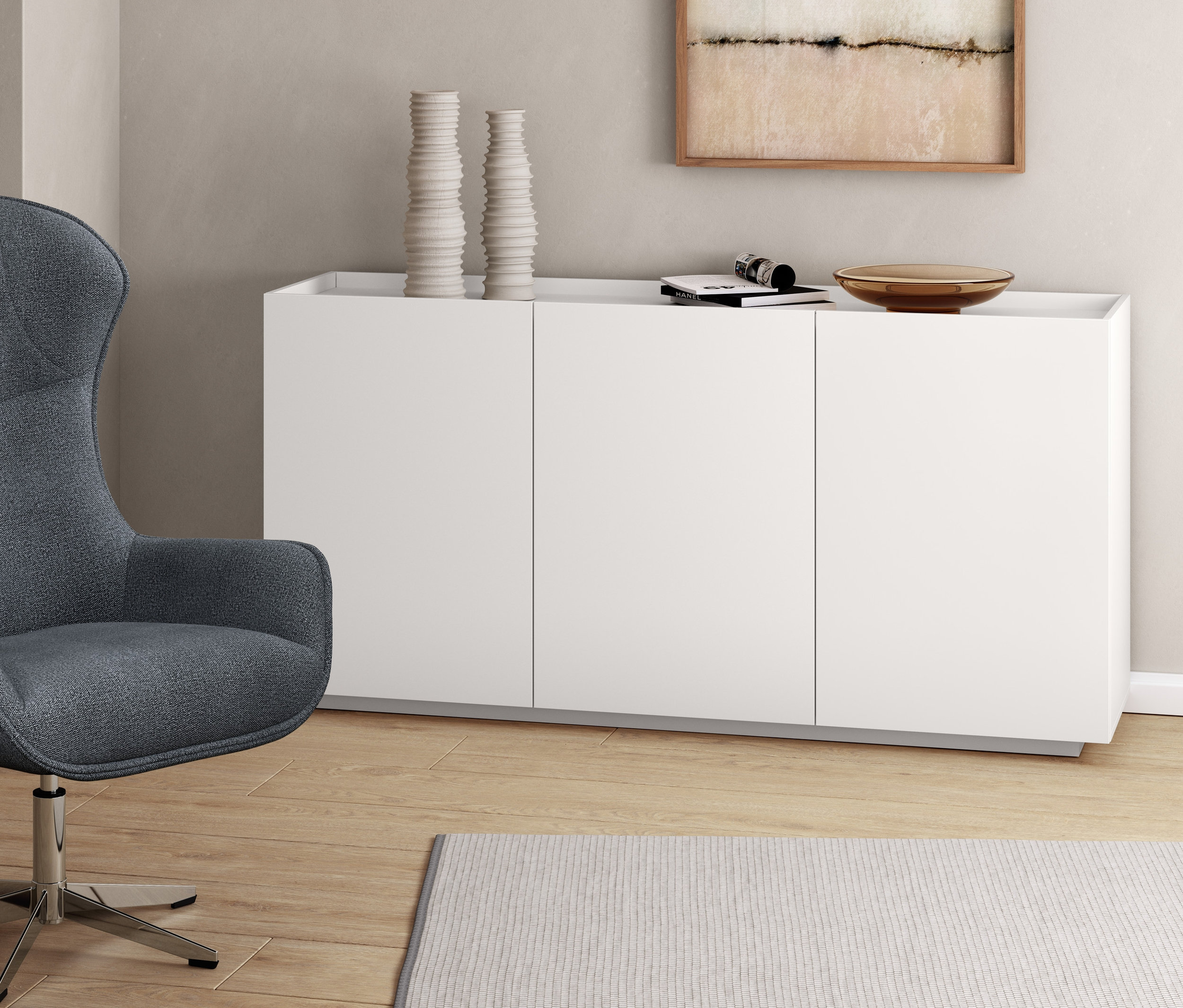 Szary fotel obrotowy obok białej szafki typu sideboard.
