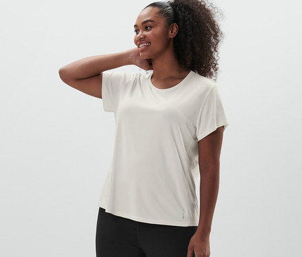 Kobieta pozuje w legginsach sportowych, czarne i koszulce funkcyjnej, złamana biel.