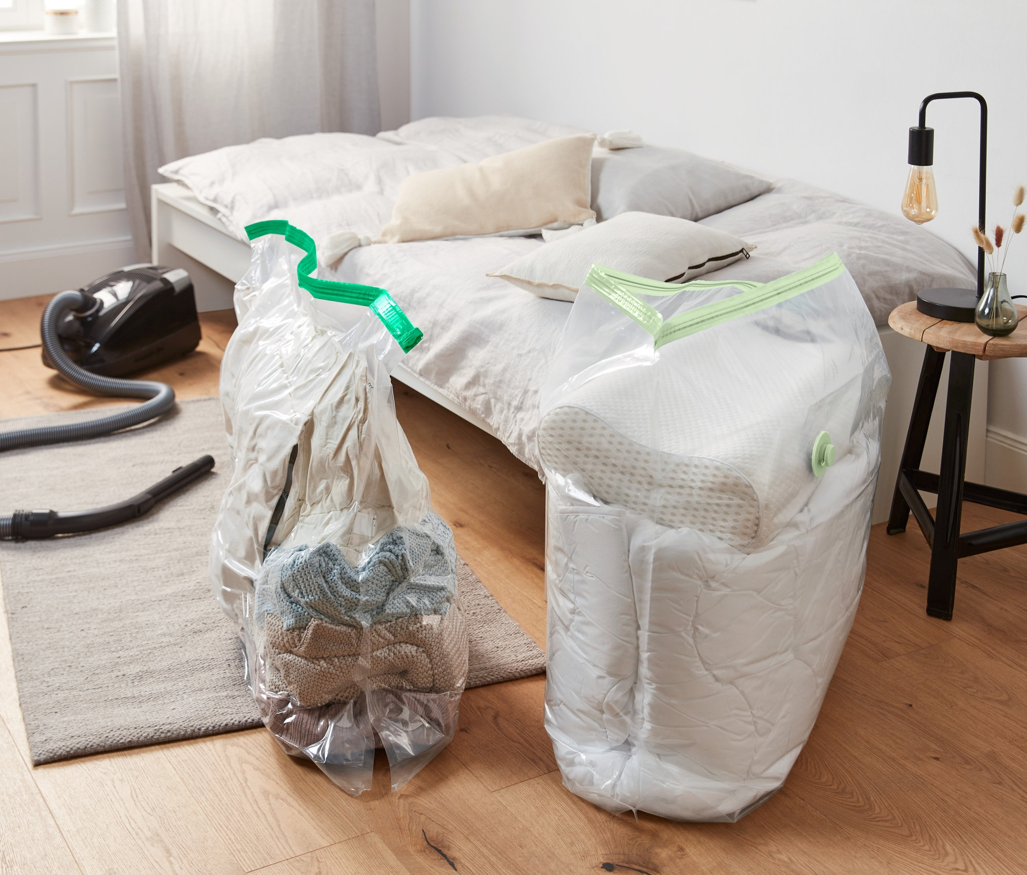 Dwa worki próżniowe w kształcie kostki leżą na podłodze obok odkurzacza i łóżka.