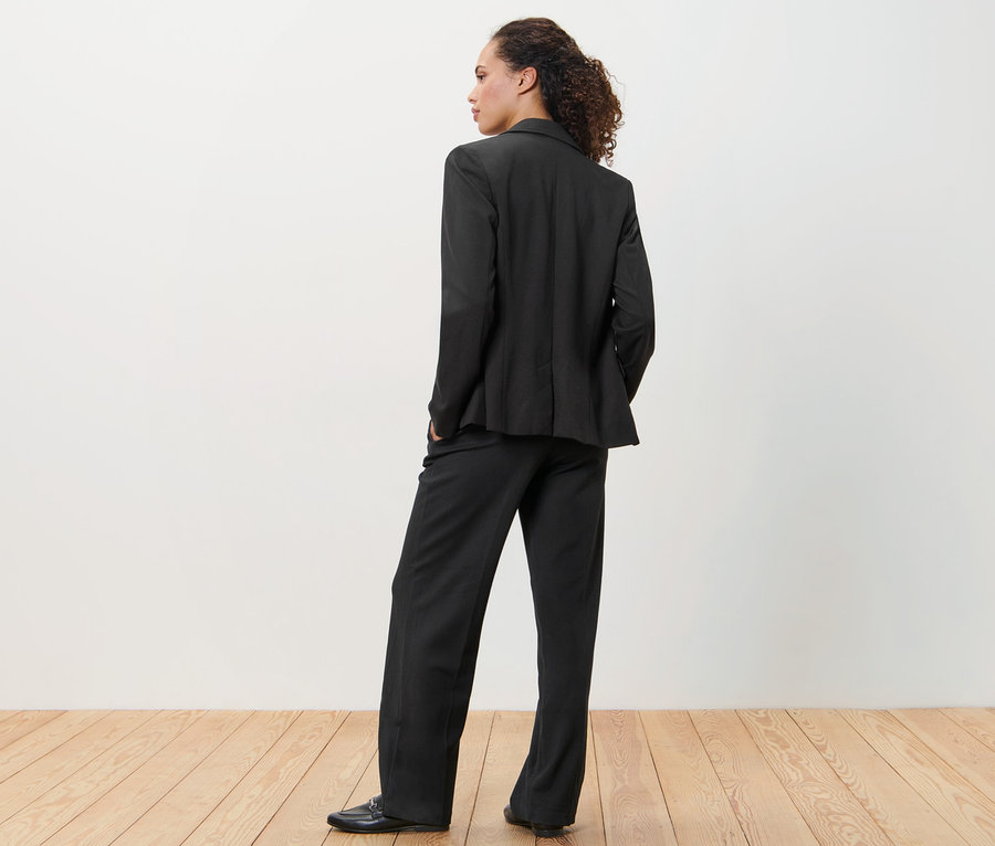 Kobieta w czarnej marynarce i spodniach z dżerseju stoi tyłem do kamery.