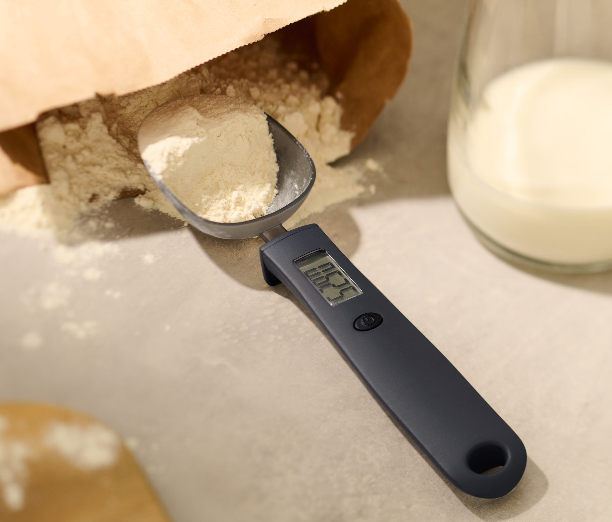 Mąka w cyfrowej wadze łyżkowej obok szklanki mleka.