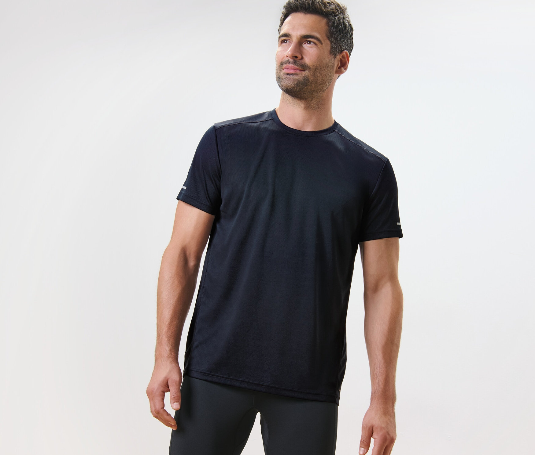 Mężczyzna w granatowej koszulce funkcyjnej stoi na jasnym tle.