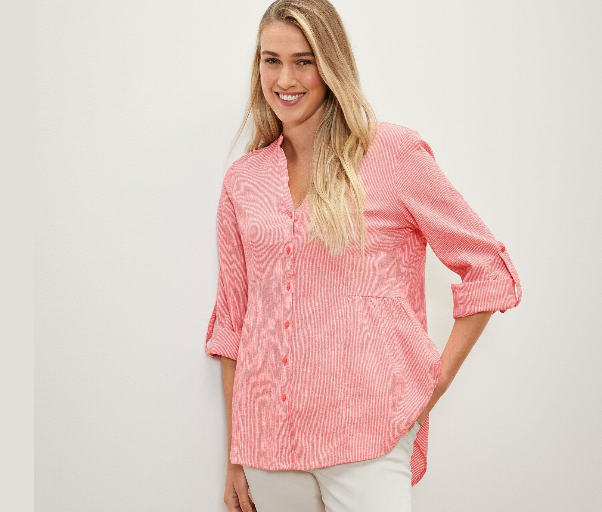 Kobieta pozuje w koralowej tunice w paski.