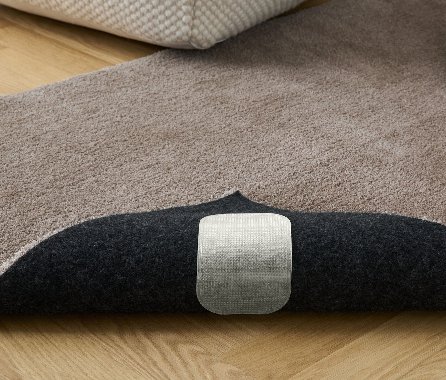 Beżowy dywan z książkami i pufem. Widoczne antypoślizgowe podkładki pod dywan, 4 sztuki.