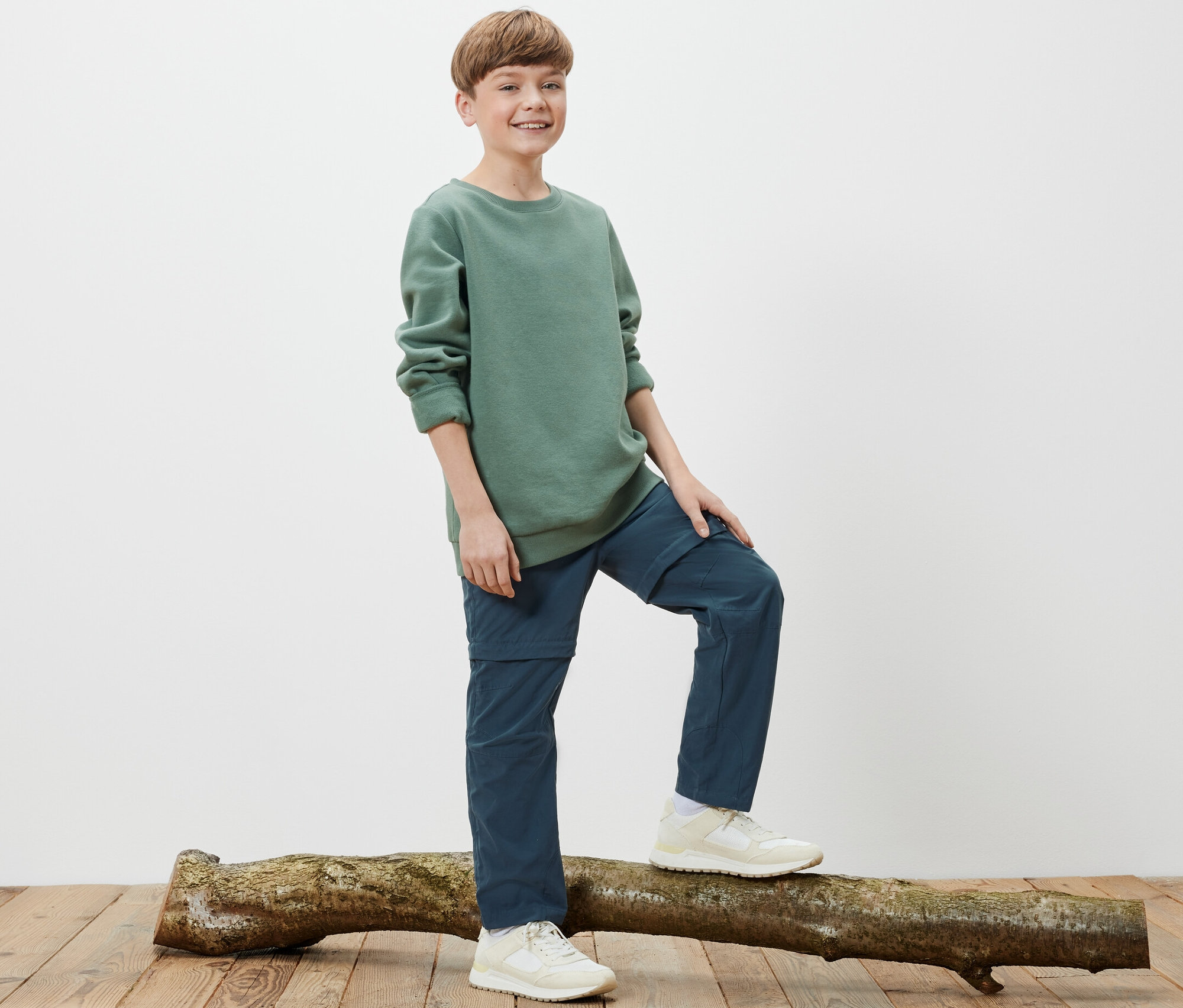 Chłopiec stoi na pniu drzewa i ma na sobie dziecięce spodnie funkcyjne.