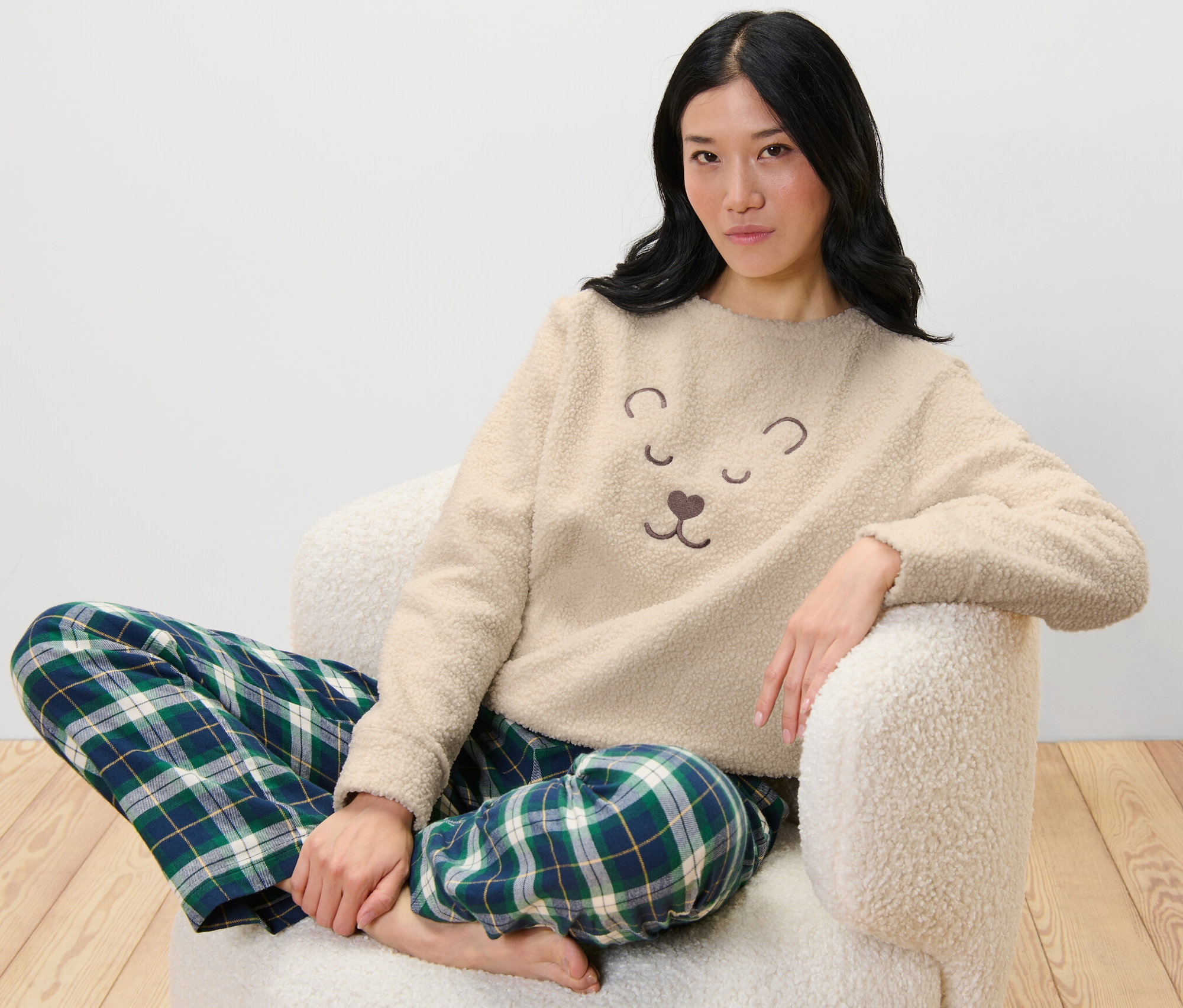 Kobieta siedzi w fotelu, ubrana w pluszową bluzę i spodnie w kratę.