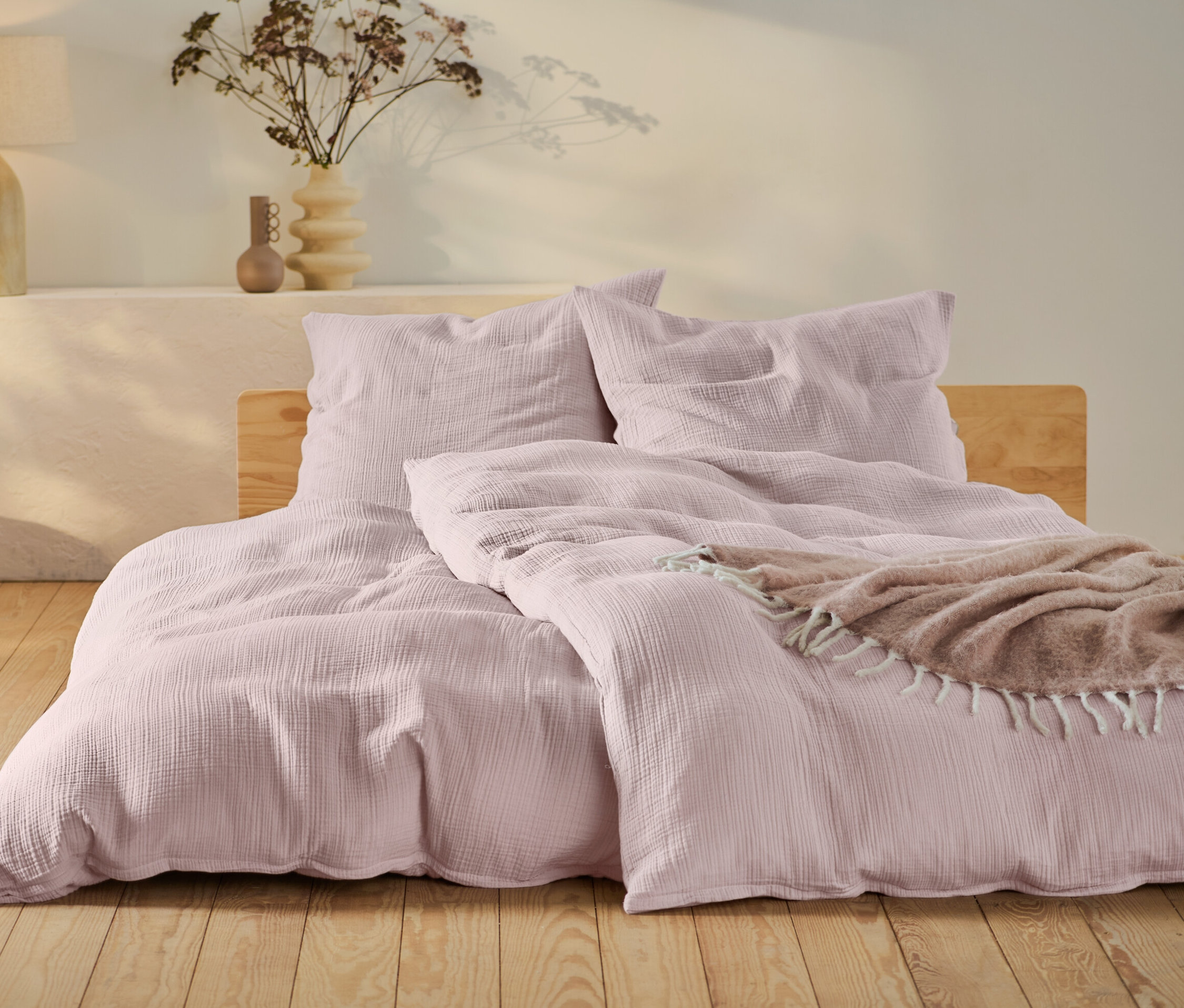 Różowa pościel muślinowa w standardowym i niestandardowym rozmiarze na łóżku z drewnianą ramą.