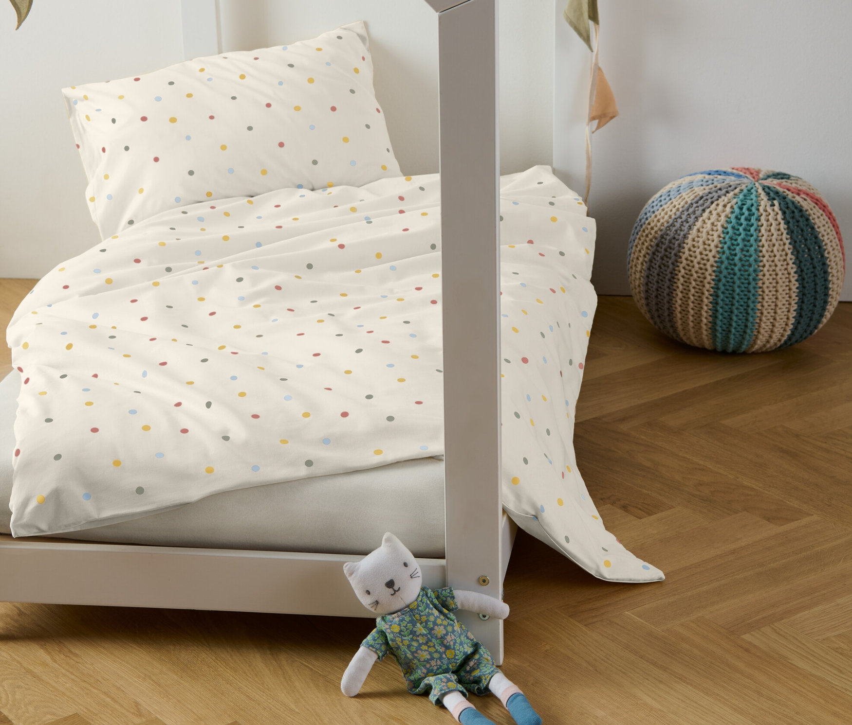 Dziecięce łóżko z pościelą dziecięcą z bawełny renforcé w kolorowe kropki, dekoracyjna girlanda i pluszowy kot.