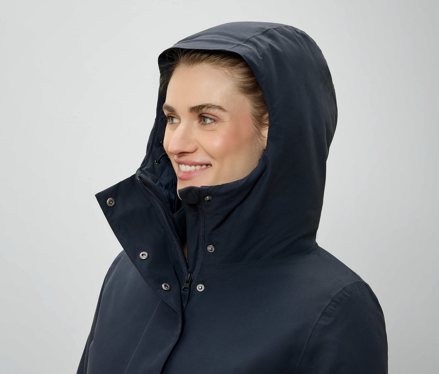 Kobieta w kapturze i granatowej kurtce patrzy w prawo.