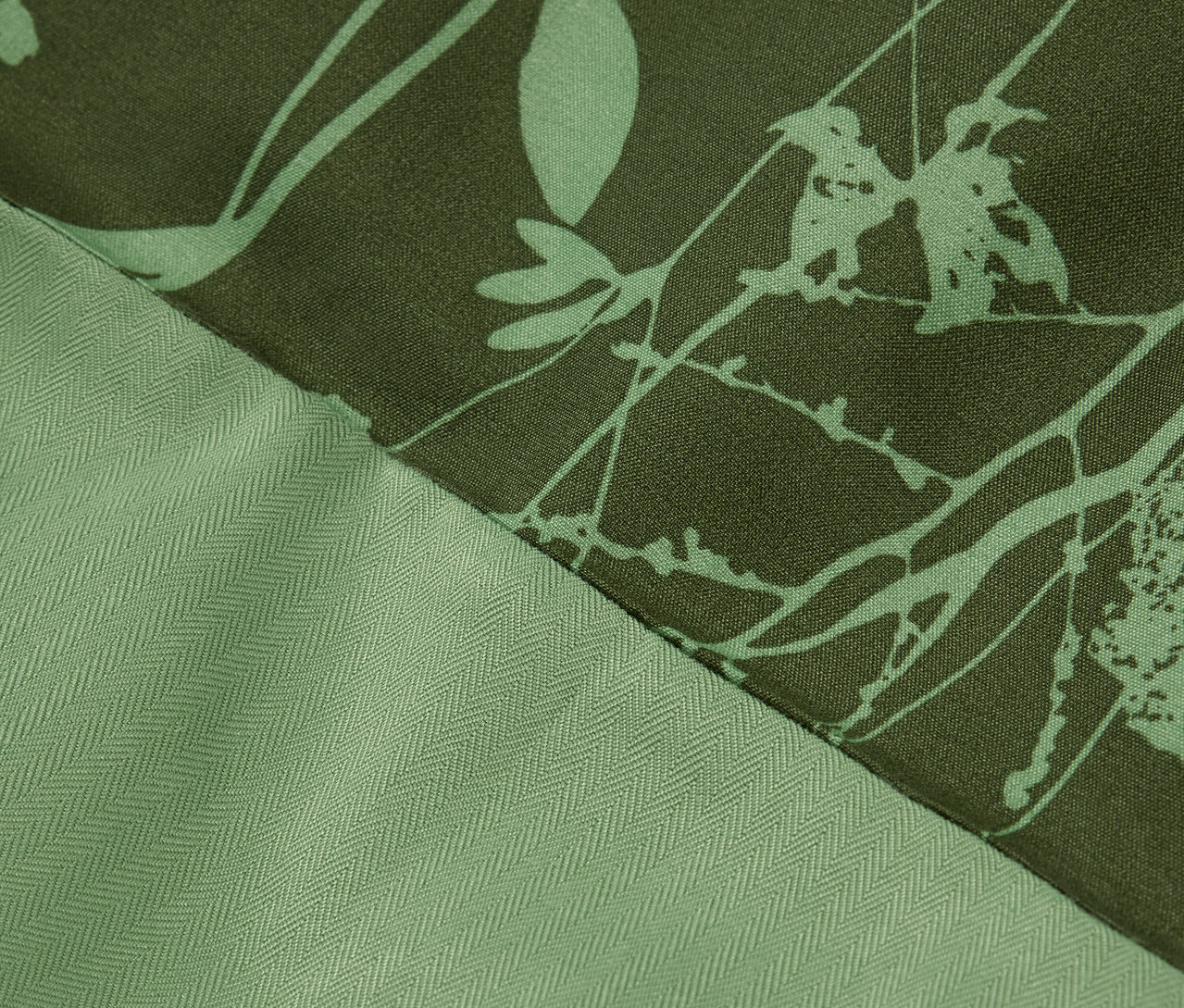 Szczegół zielonej tkaniny z kwiatowym wzorem i teksturą w jodełkę.