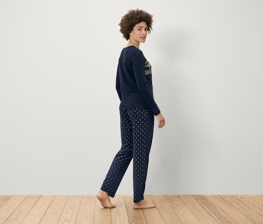 Kobieta w granatowej piżamie w białe kropki idzie po drewnianej podłodze.