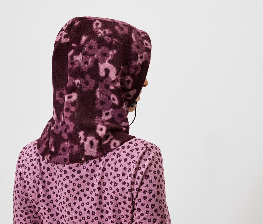 Widok z tyłu kobiety w fioletowym hidżabie w kwiaty i fioletowej koszuli we wzór serca.
