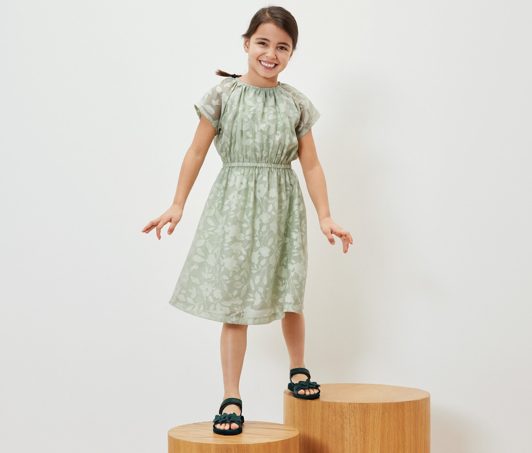 Uśmiechnięta dziewczyna stoi na drewnianych stopniach, ubrana w sukienkę.