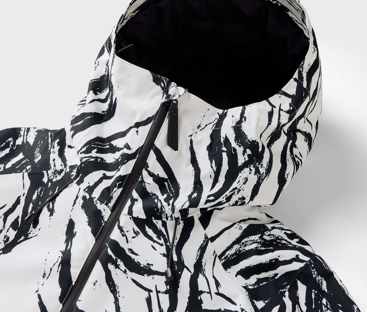 Zbliżenie na kaptur kurtki w zebrę z czarnym zamkiem błyskawicznym.