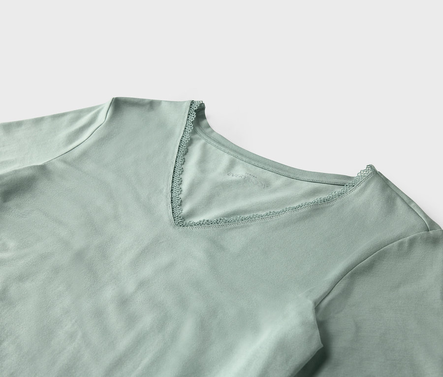 Zbliżenie jasnozielonej koszulki z krótkim rękawem i dekoltem w kształcie litery V obszytym koronką.