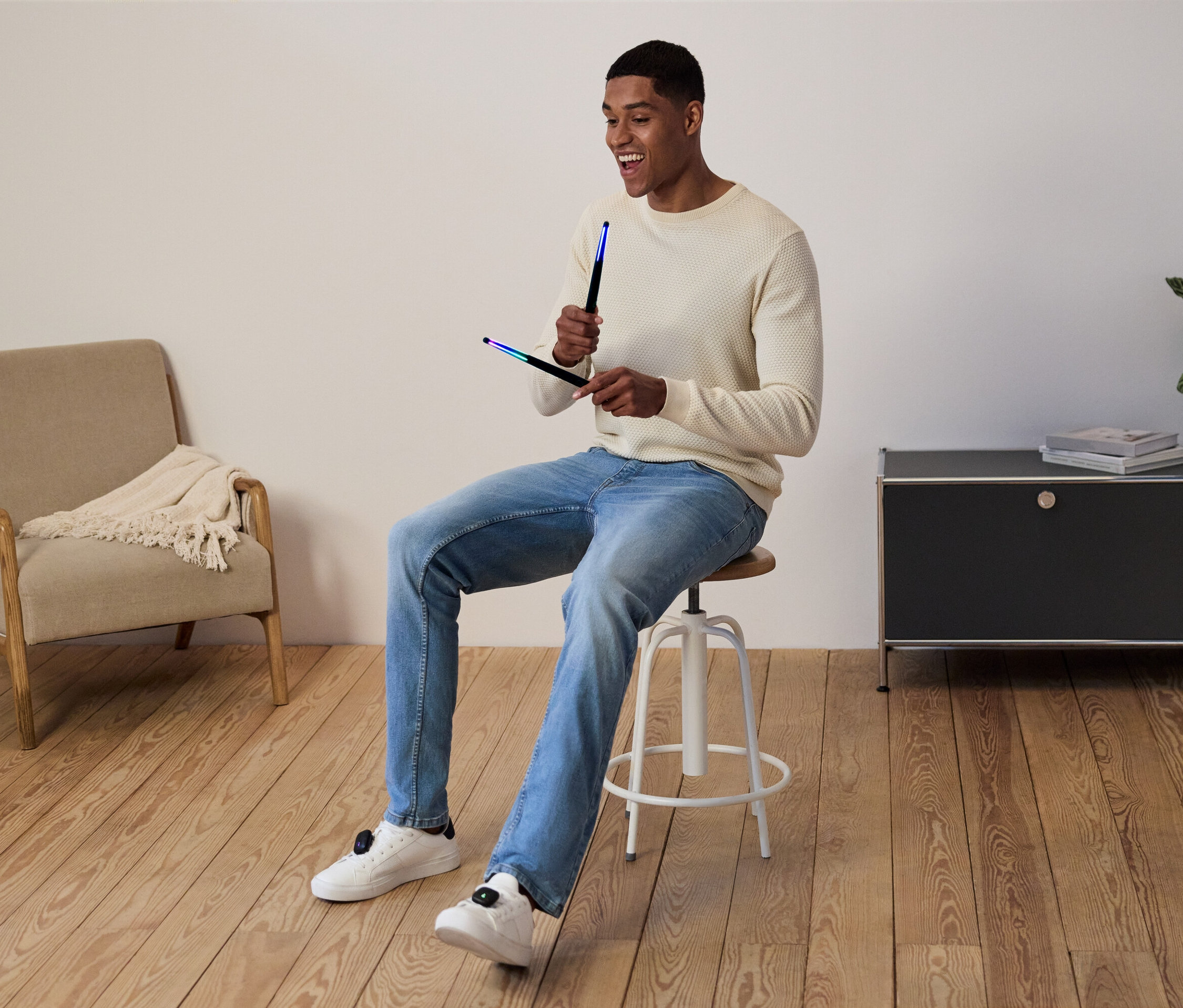 Mężczyzna siedzi na stołku i trzyma w rękach świecące pałeczki.