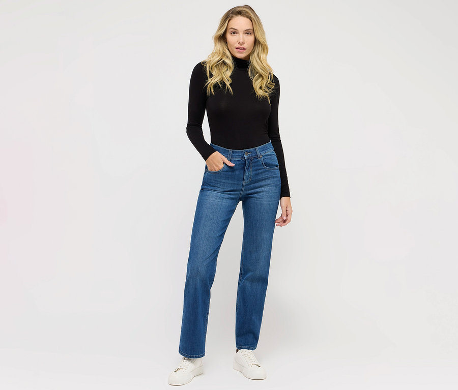 Kobieta pozuje w jeansach Angels „Lara” Straight Fit, niebieskich i czarnym golfie.